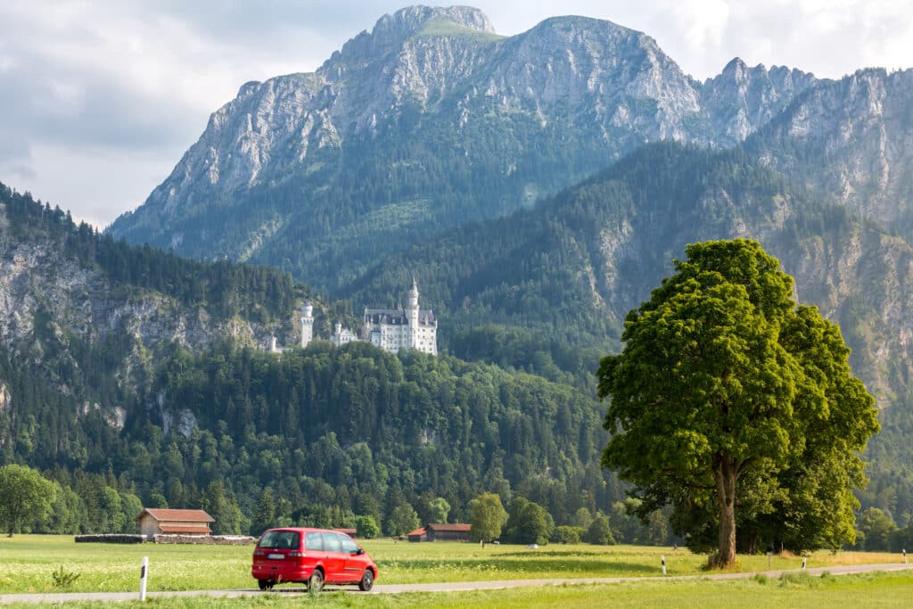 Neuschwanstein-slott og en rød bil som kjører langs bilveien.