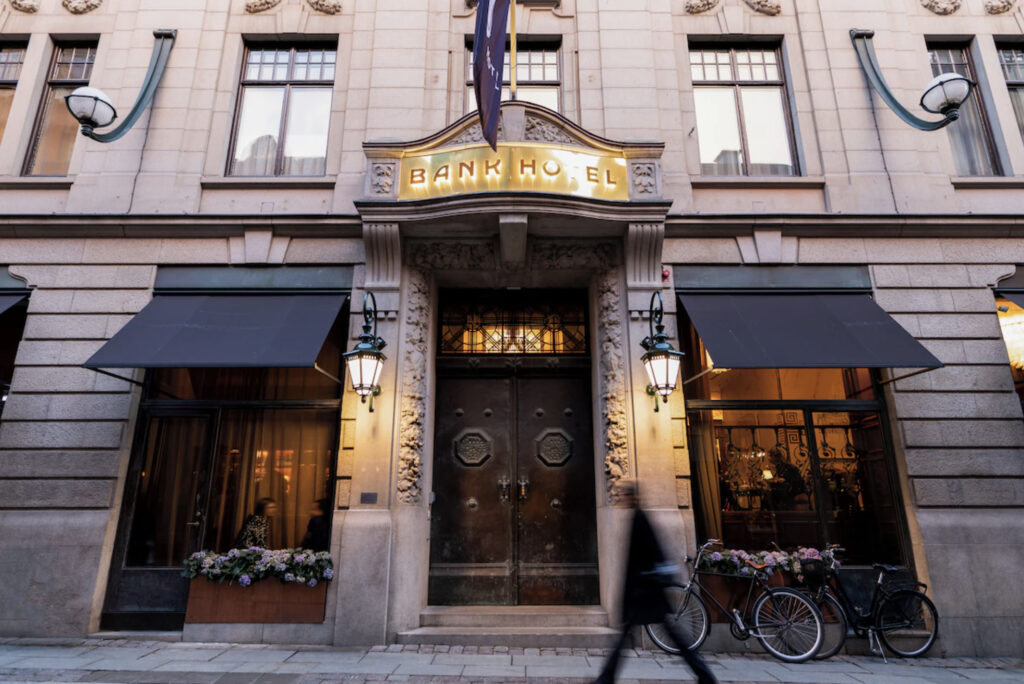 Bank Hotel med inngangsdør i svart jern, to store vinduer og sykler utenfor hoveddøra.