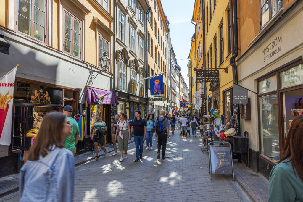 Shoppinggaten Gamla Stan med folk som går går gjennom gaten og butikker på rekke og rad. 