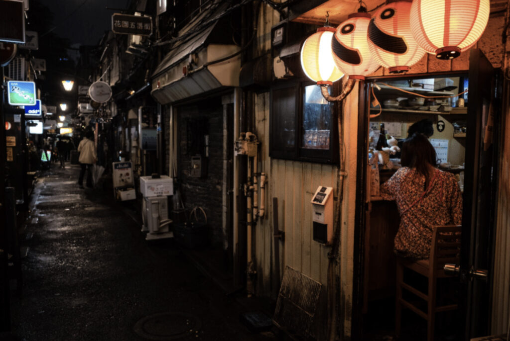 Gate i Tokyo, det er mørkt, og lampene langs døra lyser opp. Smal gate.
