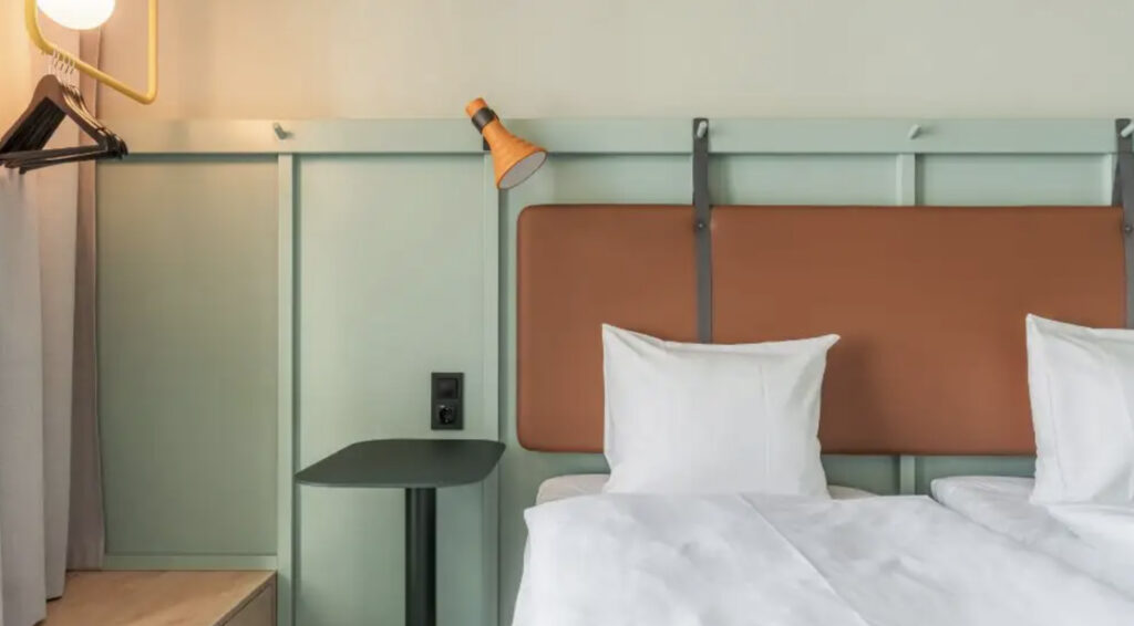 Hotellseng med lampe og grønne vegger.