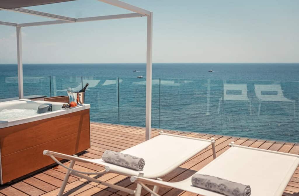 Hotell med to solsenger med utsikt over havet, og boblebad ved siden av.