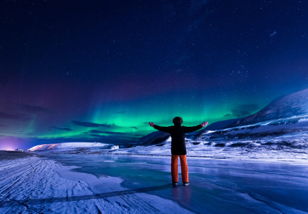 person holder ut armene under nordlyset på svalbard