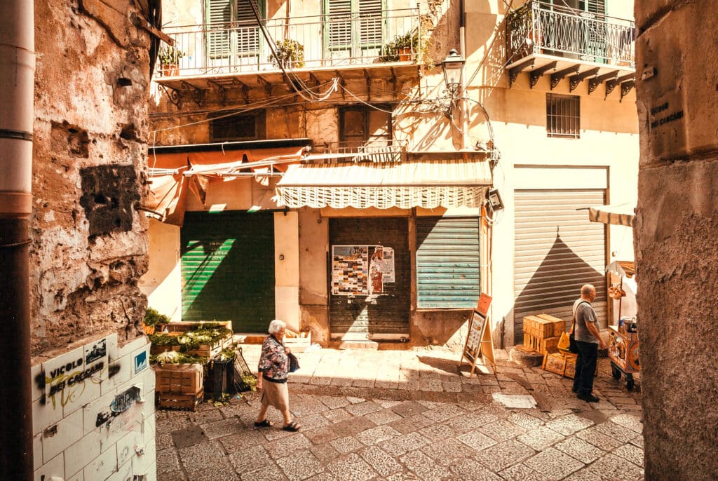 Gate i Palermo med gammel dame som går forbi. Solrik dag.