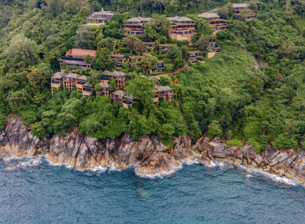 Hotellfasade midt i en grønn jungel med klipper og hav foran resort.