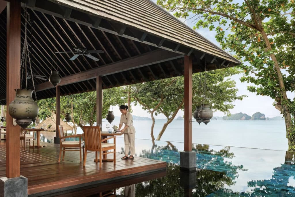 Krabi hotell med en arbeider som dekker bord på restauranten, som har utsikt mot evighetsbasseng og strand.