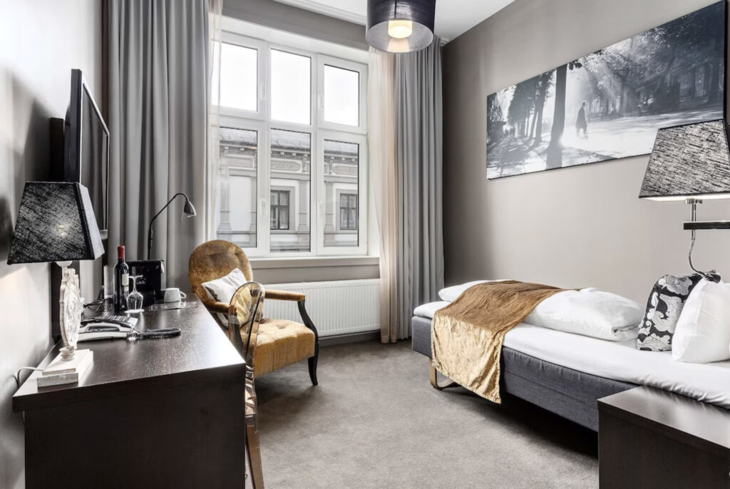 Hotellrom med enkeltseng, bilde på veggen, skrivebord og stol.