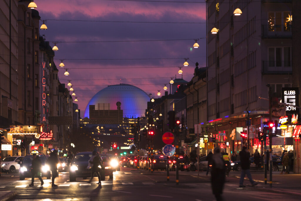 Södermalms gater om kvelden med gatelys, mennesker og biler som kjører forbi. Butikker og kino langs gatene.