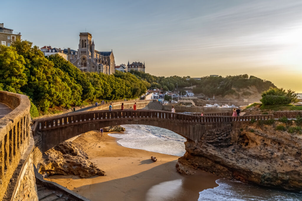 Biarritz, Frankrike. Panoramautsikt over den berømte steinbroen til Rocher du Basta, bysilhuetten og kystlinjen med sandstrender og småbåthavn. Gylden time. Ferie i Frankrike.