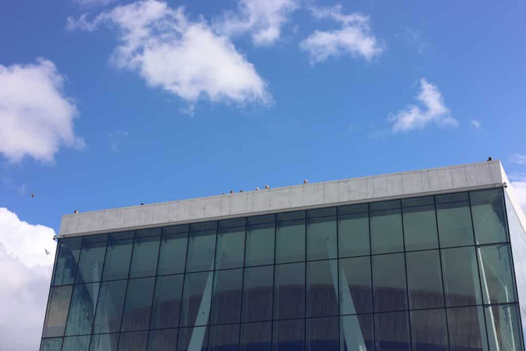 Folk som står på Opera-taket og ser ned. Blå himmel. 