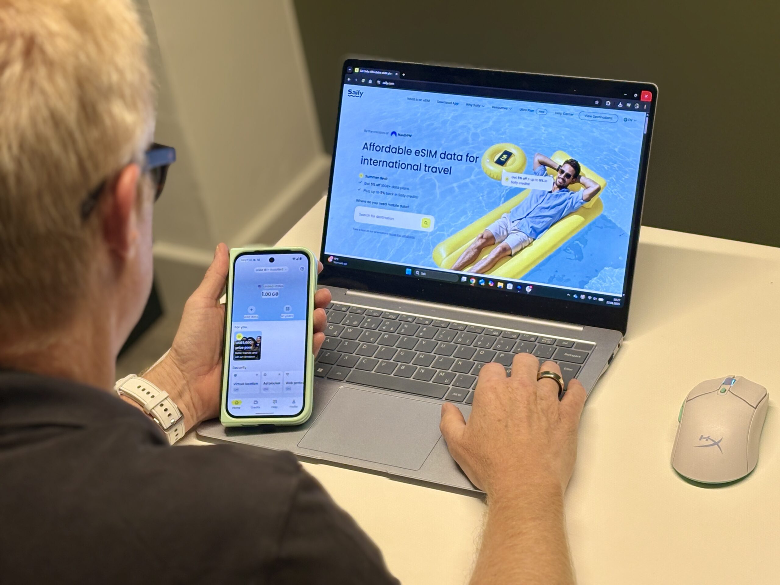 mann som sitter foran mac med en mobil i hånda