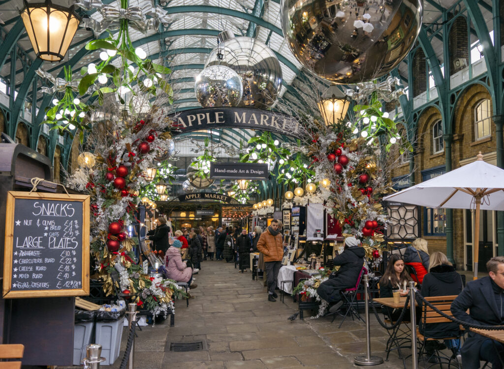 Turister, handlende og gjester på spisesteder fyller det tidligere Apple Market i Londons populære Covent Garden Market før jul. Markedet er lyst opp av festlige juledekorasjoner.