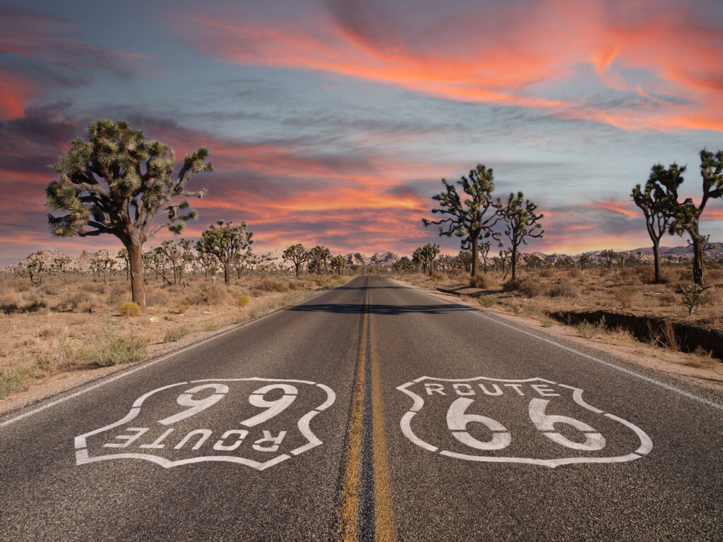 Route 66 med Joshua-trær og solnedgangshimmel i Californias Mojave-ørken.