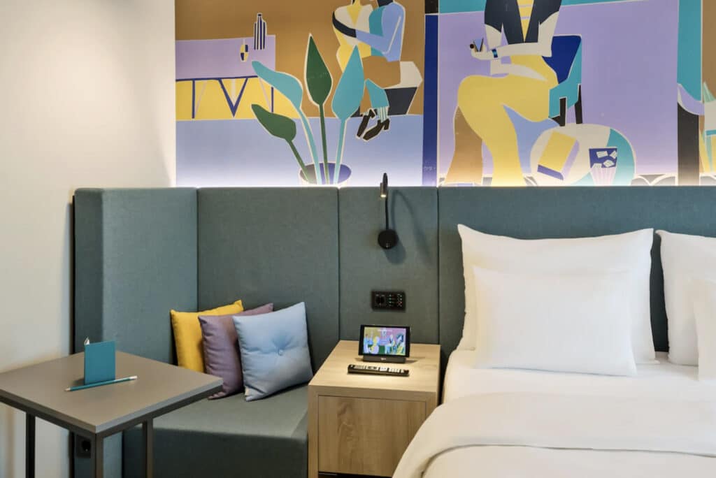 Hotellrom i hotell i Wien med dobbeltseng, liten sitteplass og fargerike malerier på veggene. 