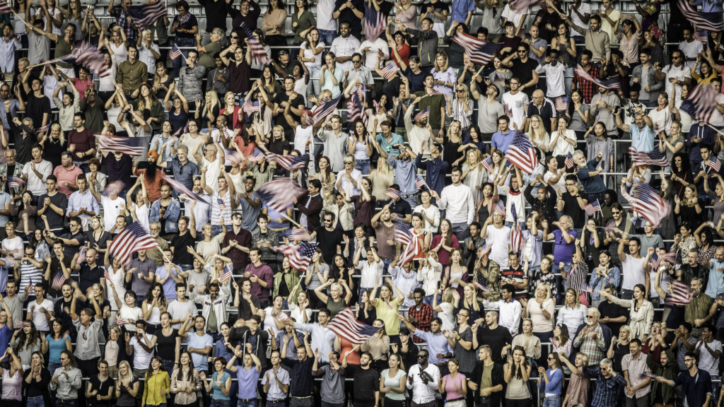 En stor folkemengde av amerikanske sportsfans heier og vaier med amerikanske flagg på tribunen.
