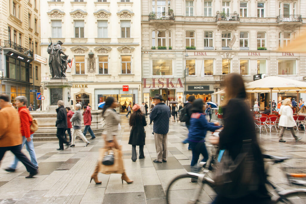 Gate med mennesker i Wien by. Bygninger og statue, dame med sykkel. 