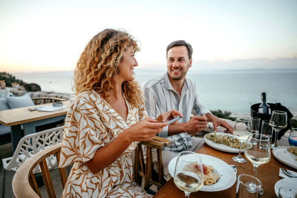 Par spiser på en restaurant med havet i bakgrunnen og utsikt